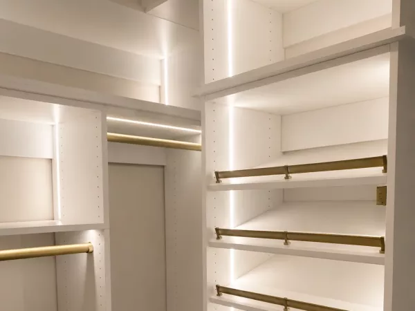 Luxury custom closet with LED-lit shelving, brass closet rods and angled shoe display by TopSouth Countertops and Closets in Marietta, GA