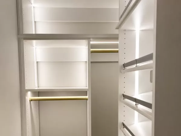 Small walk-in closet with LED lighting, brass hanging rods and angled shoe shelves by TopSouth Countertops and Closets in Atlanta, GA